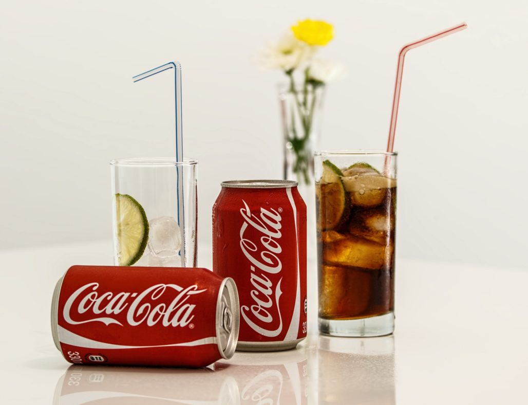 Two cans of Coca-Cola on a table next to filled glasses
